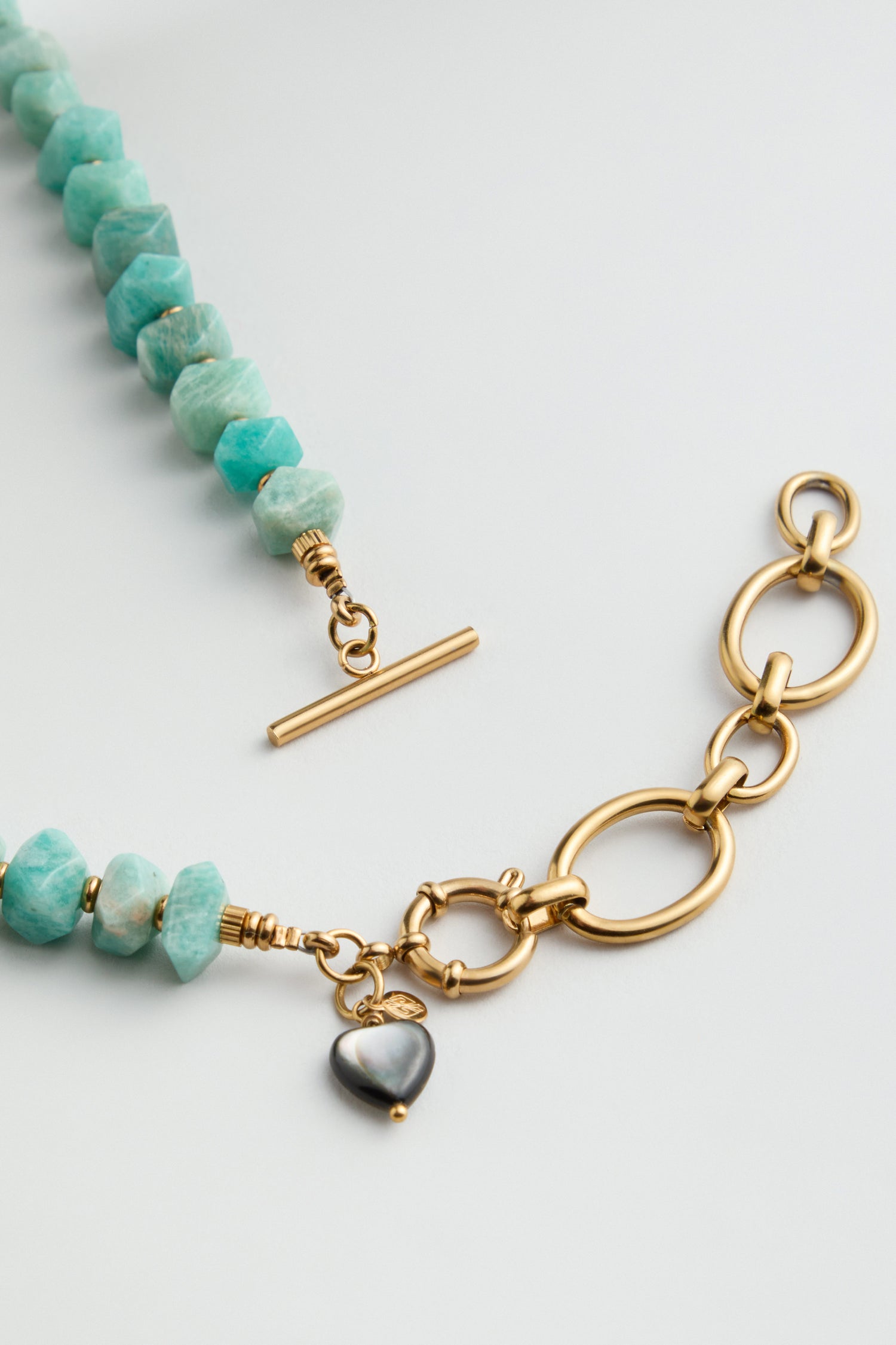 The Amazonite Bead Necklace features turquoise and amazonite gemstone beads on one side, large gold links on the other, a gold toggle clasp, and a small heart-shaped charm.