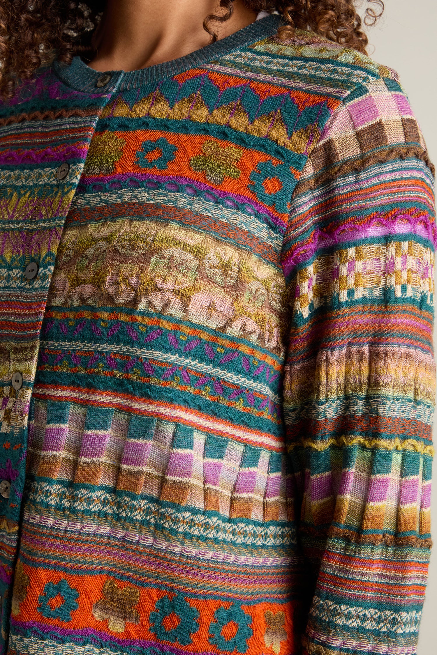 Close-up of a person wearing a vibrant Round Neck Button Cardigan featuring an intarsia knit design with intricate geometric shapes and floral motifs.