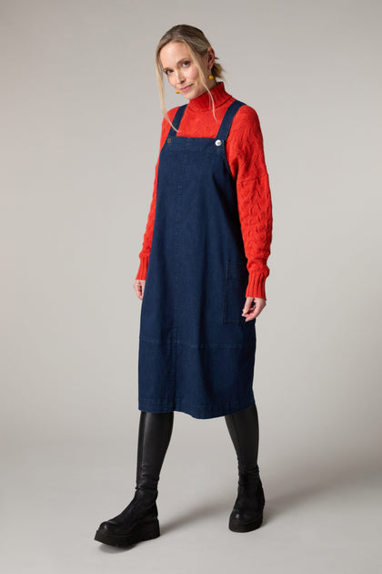 A woman wearing a blue Stretch Denim Pinafore Dress and a red turtleneck.