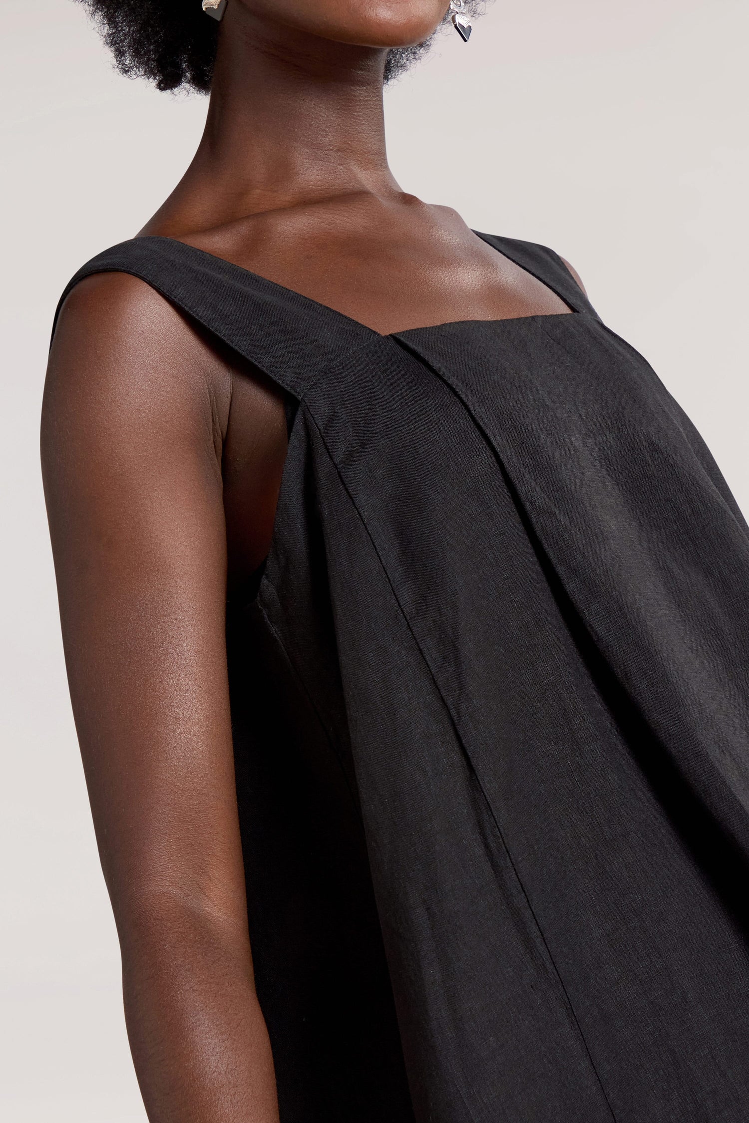 A close-up of a person wearing a black, sleeveless Square Neck Bubble Linen Dress with wide shoulder straps. The pure linen fabric and square neckline make it perfect for any summer rotation. The background is a plain, light color.