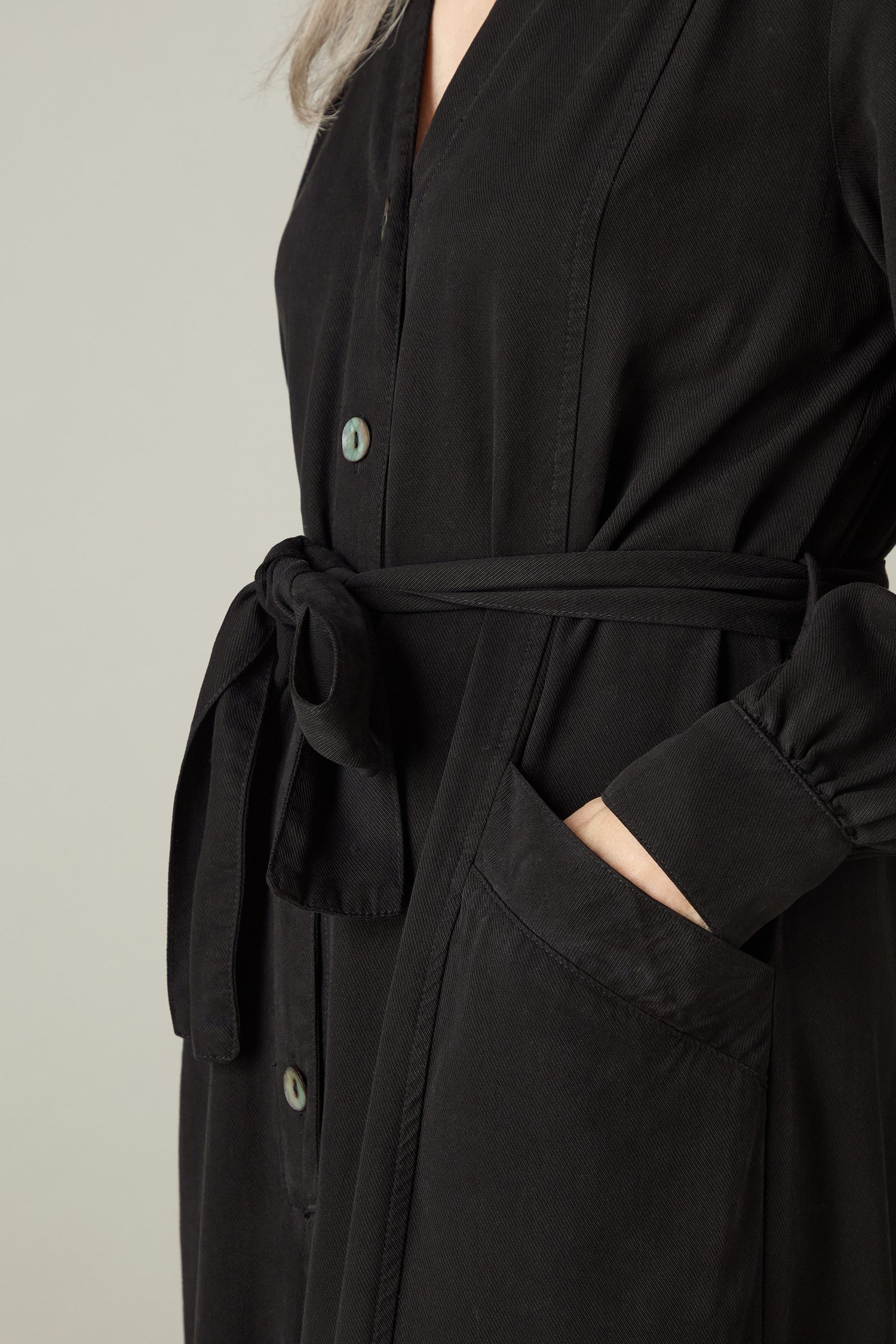 A person wearing a black Fluid Twill Jumpsuit crafted from eco-friendly fabric, featuring a tied waist belt.