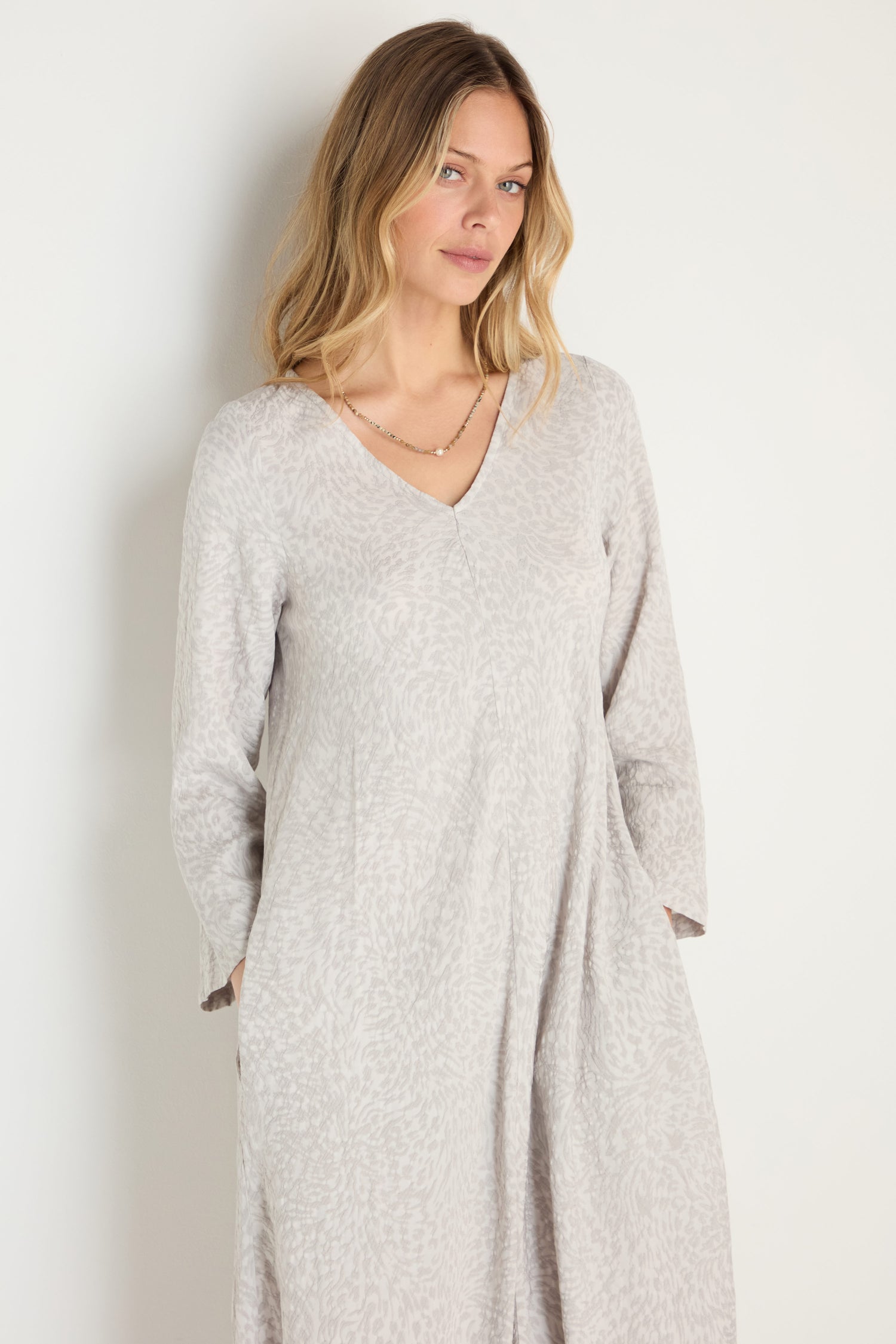 A woman with long blonde hair wears the Animal Textured Jacquard Maxi Dress in light gray with long sleeves and a simple necklace, standing against a plain white background.
