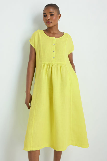 A person models the Linen Button Lemon Placket Dress, featuring a loose fit, short sleeves, buttoned front, and midi length in yellow linen, standing against a white background for an effortlessly elegant look.