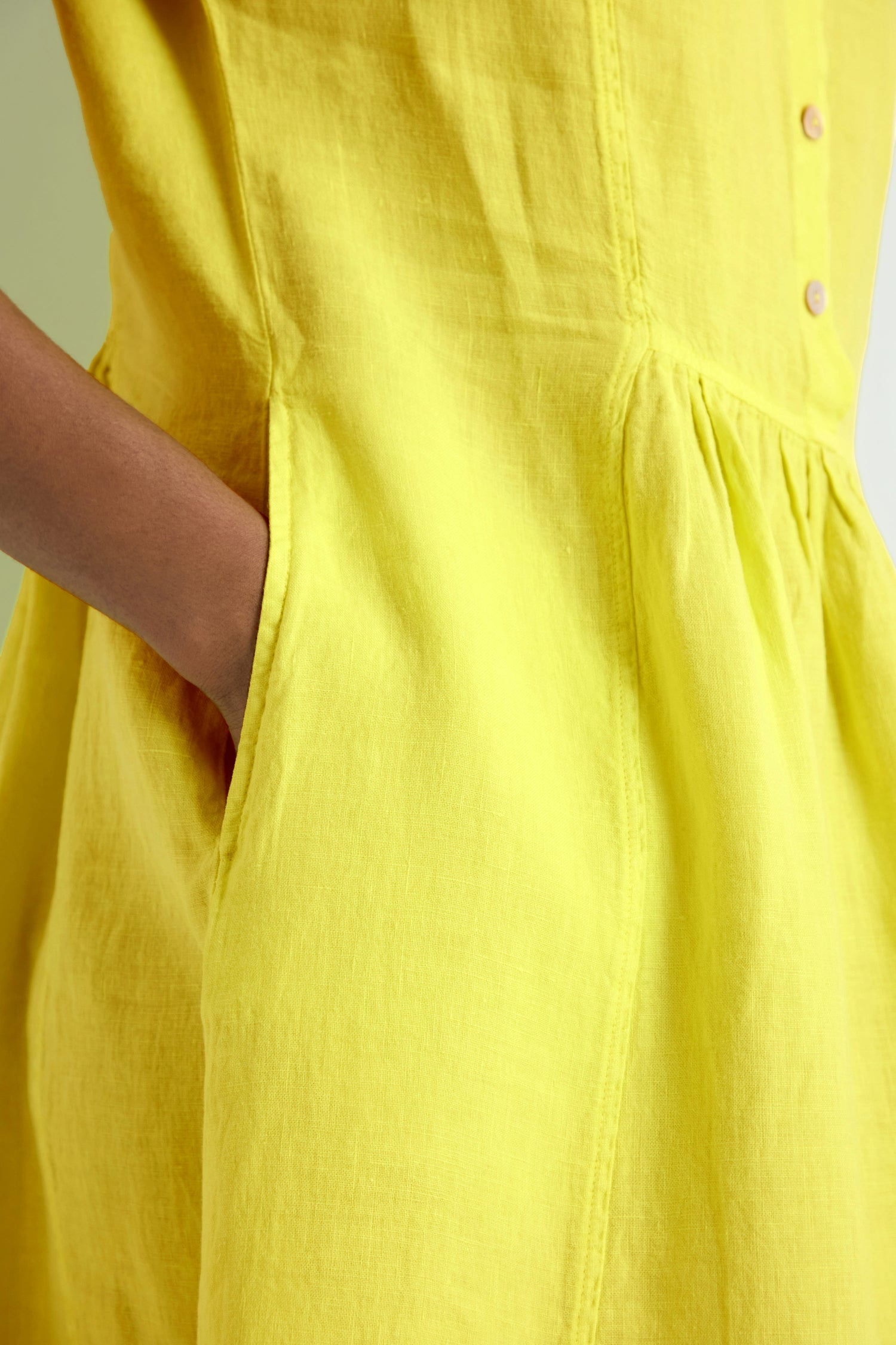 Close-up of a person wearing the Linen Button Lemon Placket Dress, a yellow fit and flare midi with visible stitching, front buttons, and side pockets.
