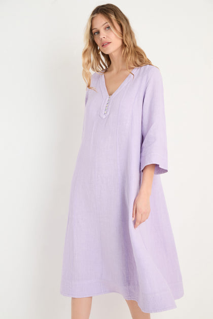 A woman in the Linen Seam Pansy Flare Dress, a light purple linen flare dress with panel seams and three-quarter sleeves, stands against a plain white background.