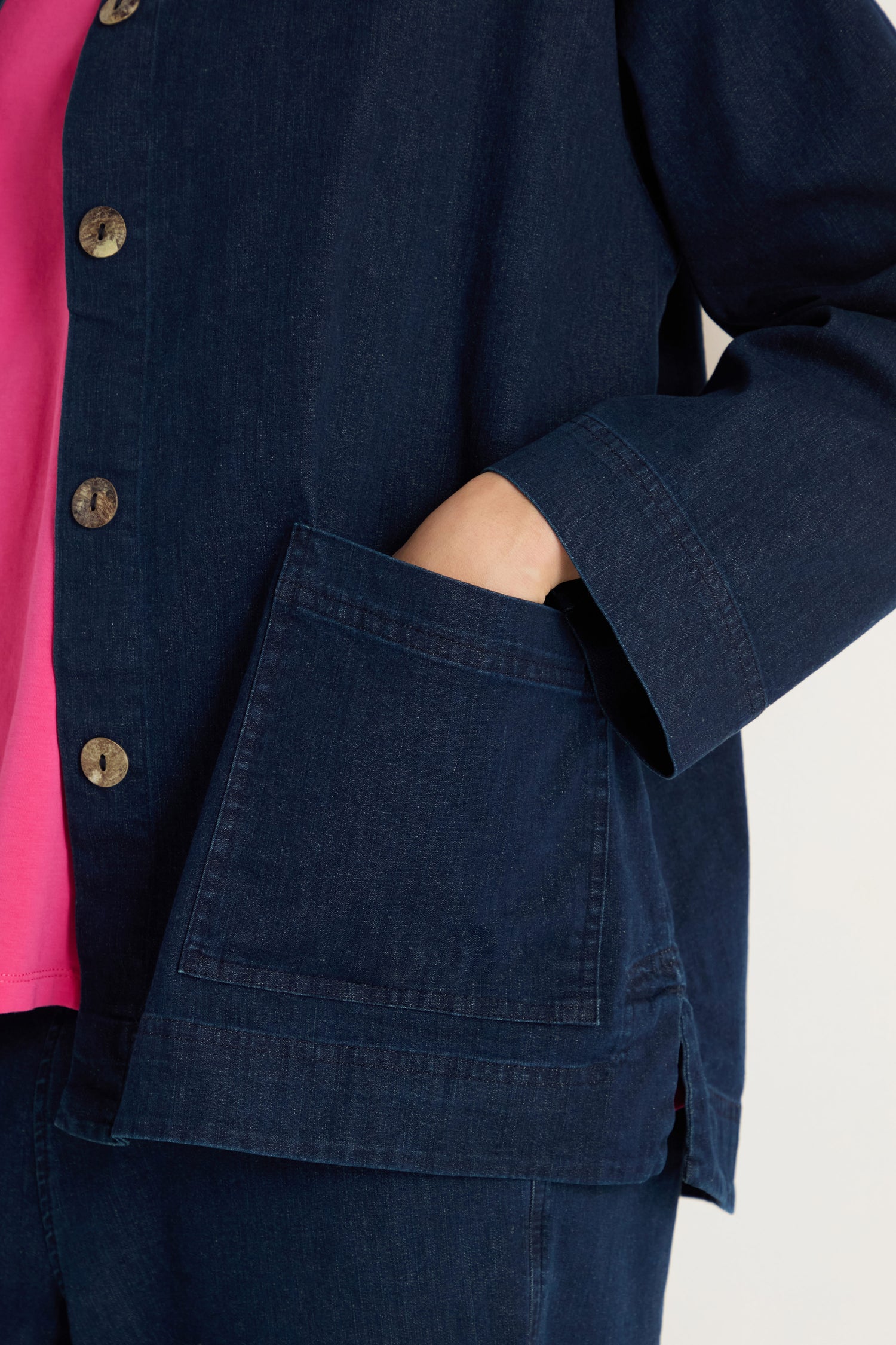 Person wearing the Stretch Denim Boxy Jacket, a dark, relaxed fit denim piece featuring large buttons and a front pocket with their hand partially inside; a pink shirt shows underneath.