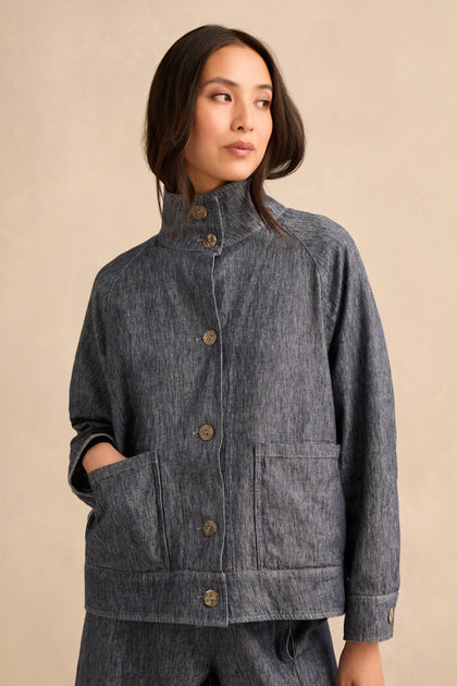 A woman wearing the Washed Cotton Linen Jacket in gray, featuring large pockets and paired with matching pants, stands against a plain beige background, gazing off to the side.