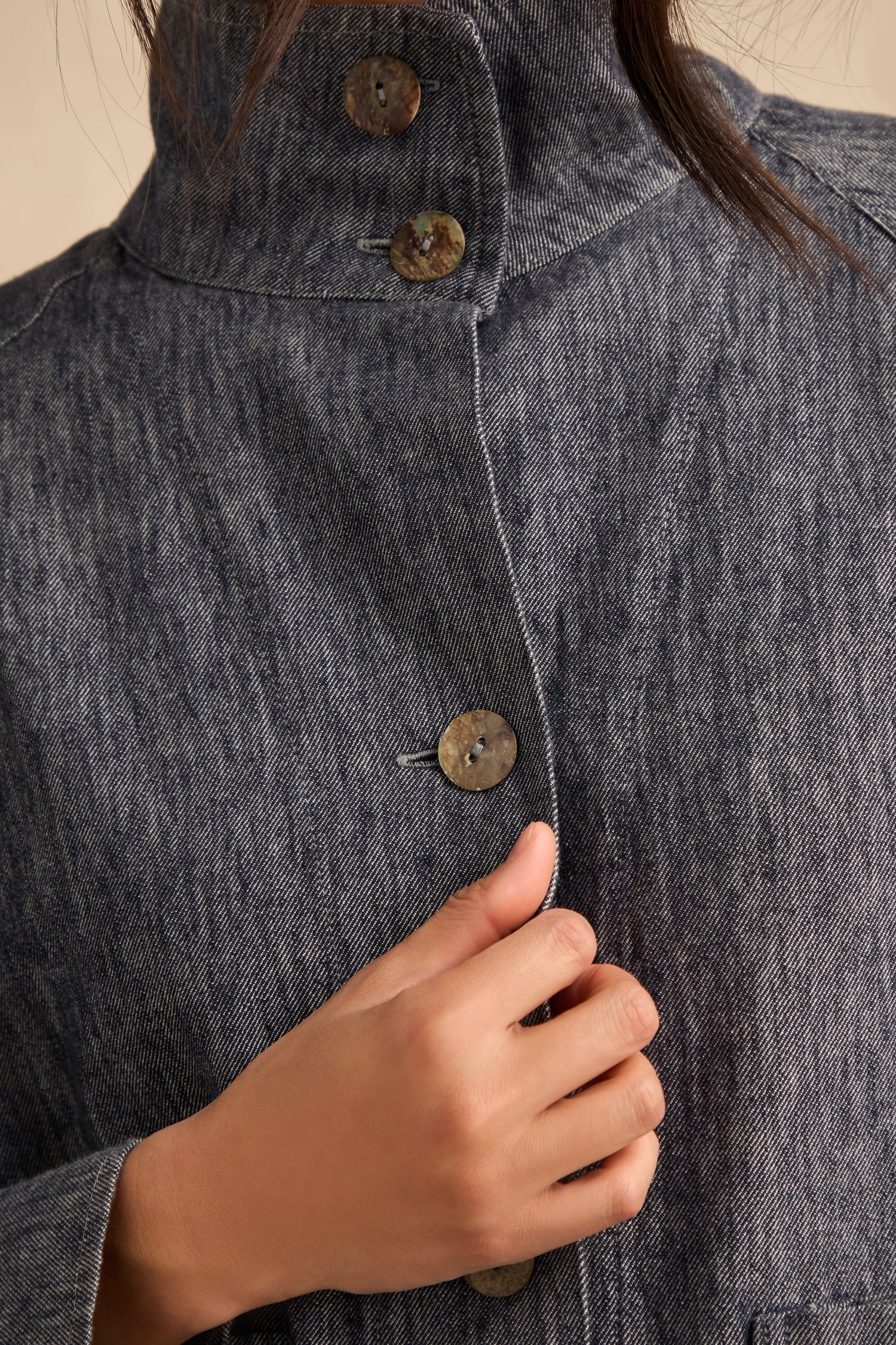 A person wearing the Washed Cotton Linen Jacket in grey, featuring a high collar and button-up design, holds the front near their chest with their right hand.