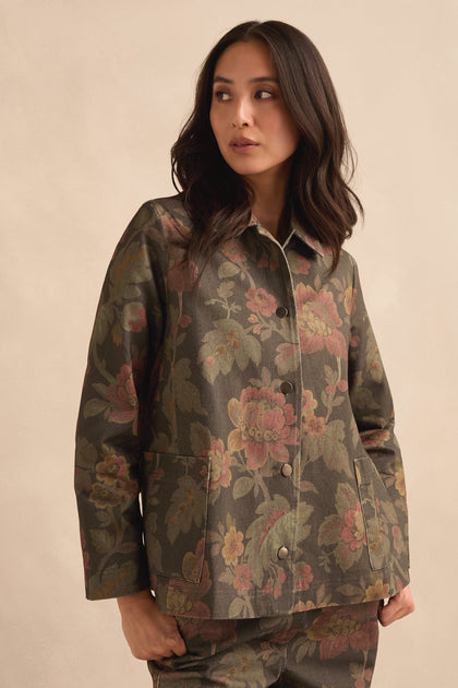 A woman wearing the Heirloom Damask Denim Jacket with a dark archive print and matching pants stands against a light beige background, looking to the side.