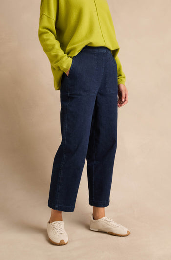 Person wearing a loose lime green sweater, Stretch Denim Blue Straight Trousers, and white sneakers, standing against a beige background.