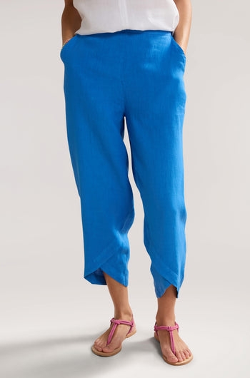 A person stands wearing blue Linen Bubble Trouser with hands in pockets and pink sandals, epitomizing the perfect summer staple from the waist down.