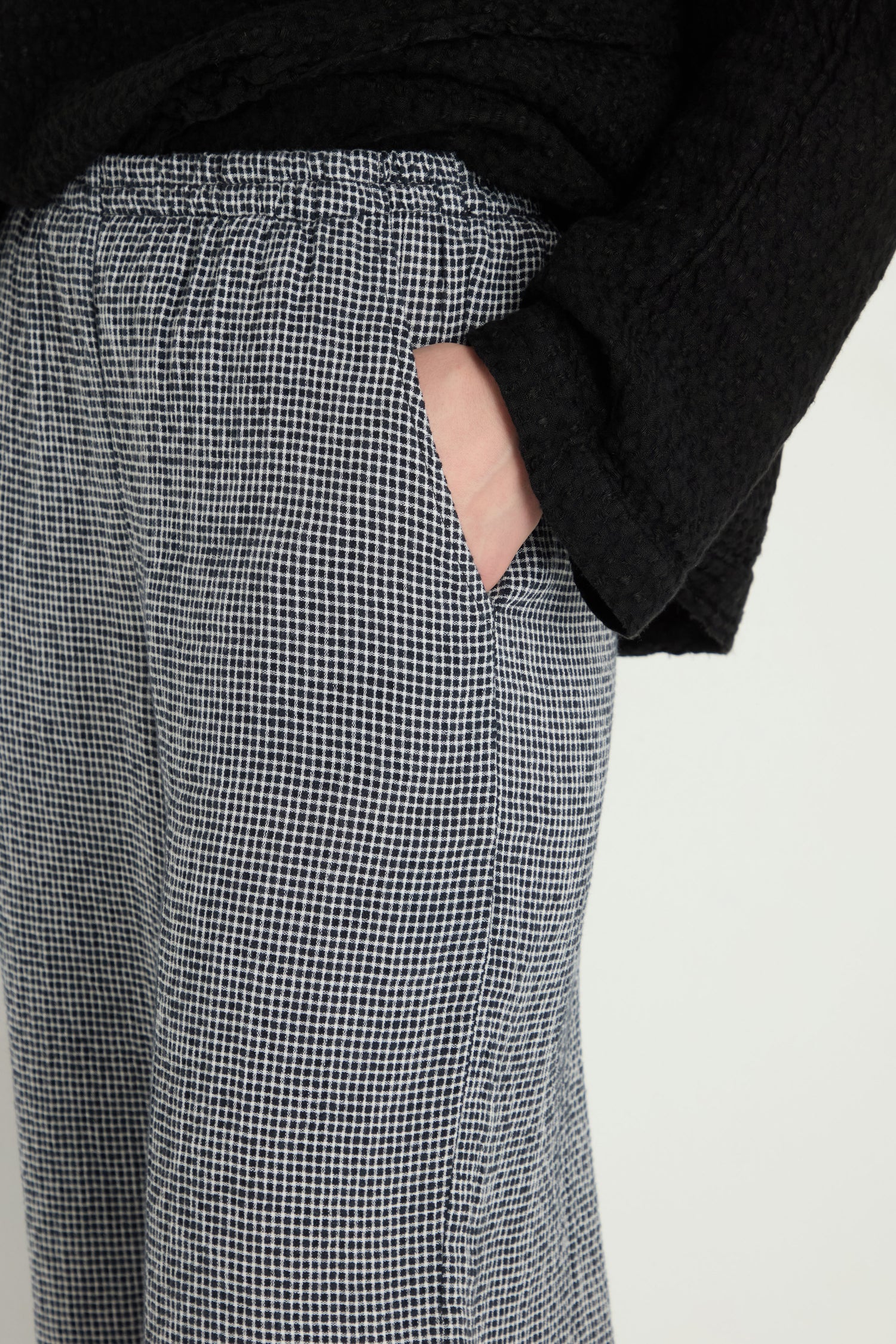 A person wearing a black top and Micro Gingham Bubble Trouser stands with one hand in their pocket.