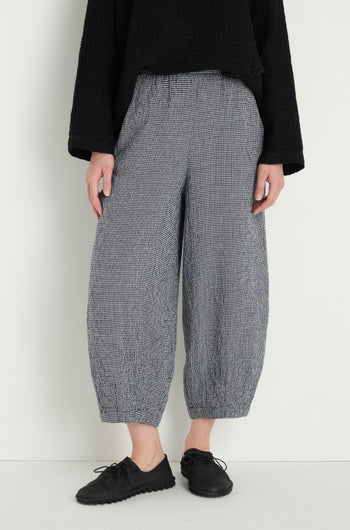 A person stands against a white wall wearing the MTP5167-MGI black textured long-sleeve top, Micro Gingham Bubble Trouser, and black lace-up shoes.