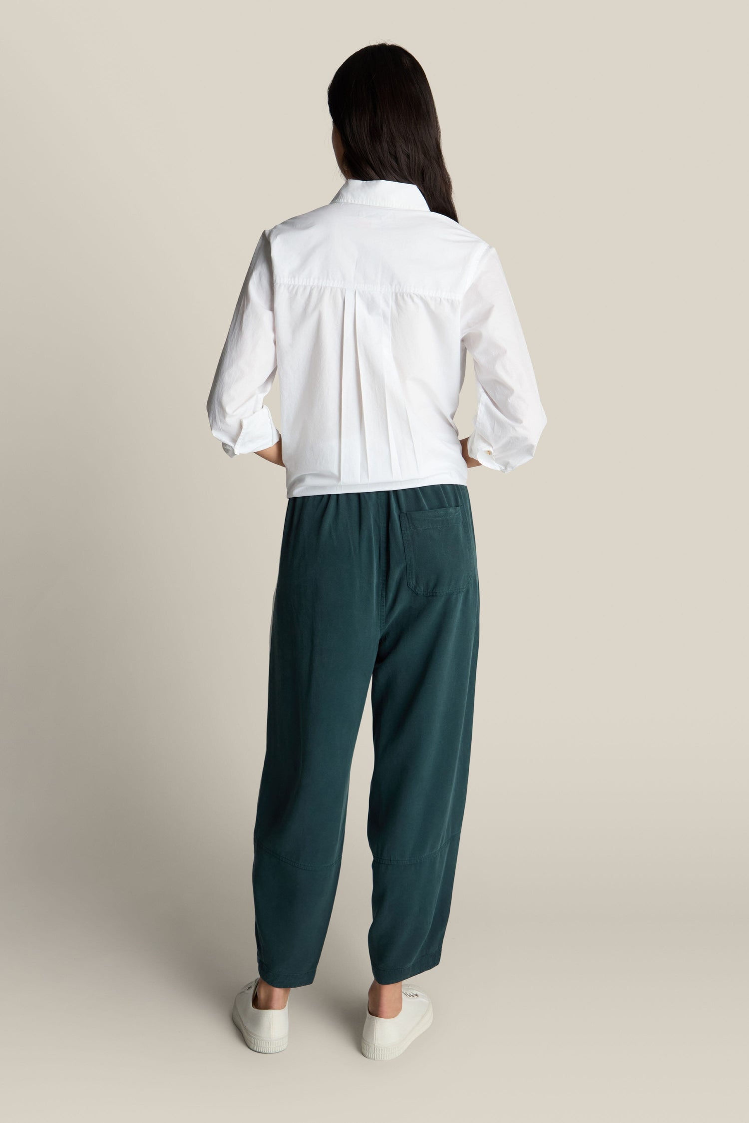 A person wearing a white long-sleeve shirt and teal Fluid Twill Bubble Trouser with an elasticated waist, is standing with their back facing the camera.