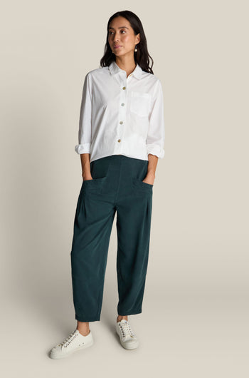 A person is standing with hands in pockets, wearing a white button-up shirt, dark green Fluid Twill Bubble Trousers with an elasticated waist, and white sneakers, on a plain light background.