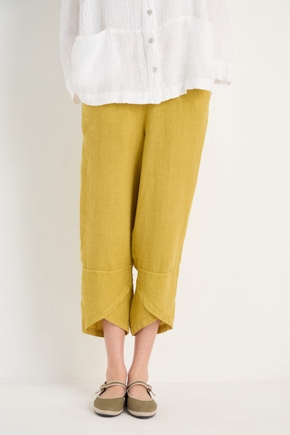 Person wearing a white textured shirt, Linen Tulip Hem Golden Bubble Trousers in mustard yellow, and brown Mary Jane shoes, standing against a plain light background.