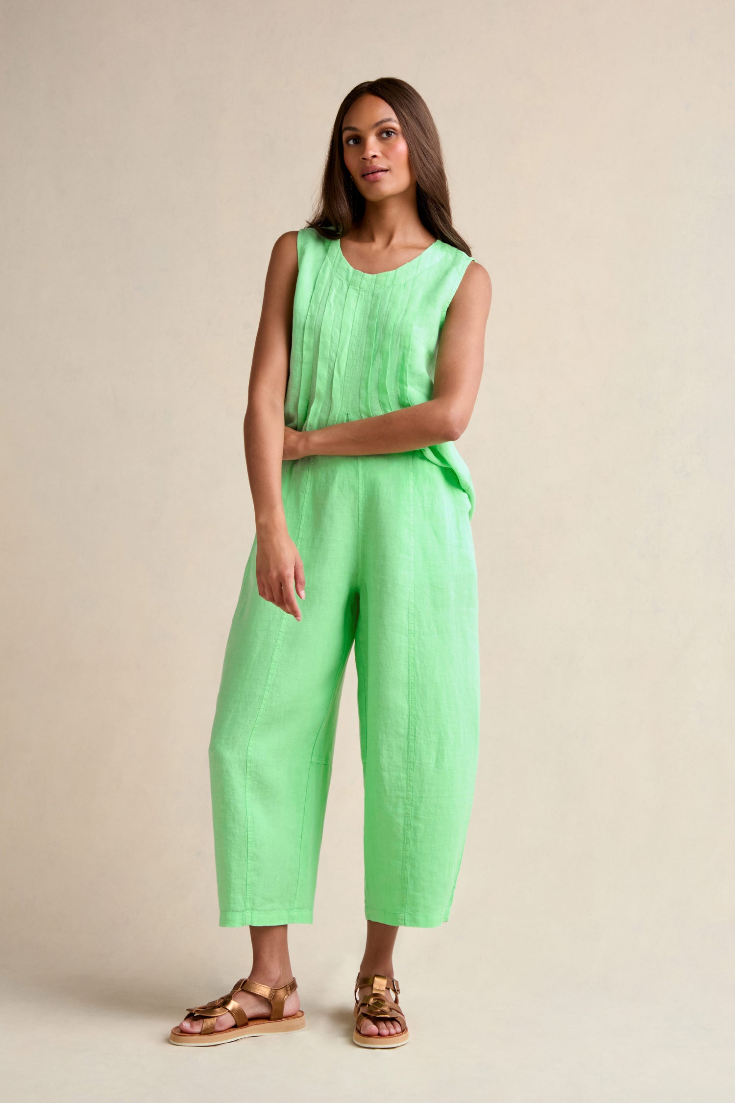 A woman stands against a plain background wearing a sleeveless light green top, gold sandals, and the Linen Seam Detail Pistachio Bubble Trouser featuring an elasticated waistband.