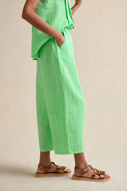A person stands with one hand in their pocket, wearing the Linen Seam Detail Pistachio Bubble Trouser with an elasticated waistband and brown sandals against a neutral background.