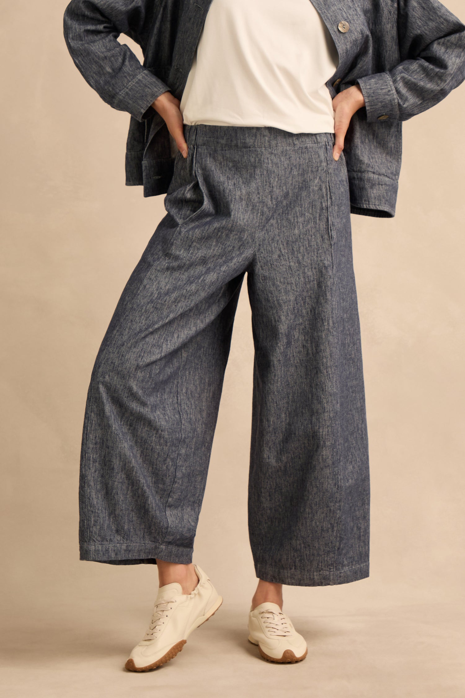 A person wearing Washed Cotton Linen Barrel Trousers with an elasticated waist, paired with a matching jacket, white t-shirt, and white sneakers stands with hands on hips against a neutral background.
