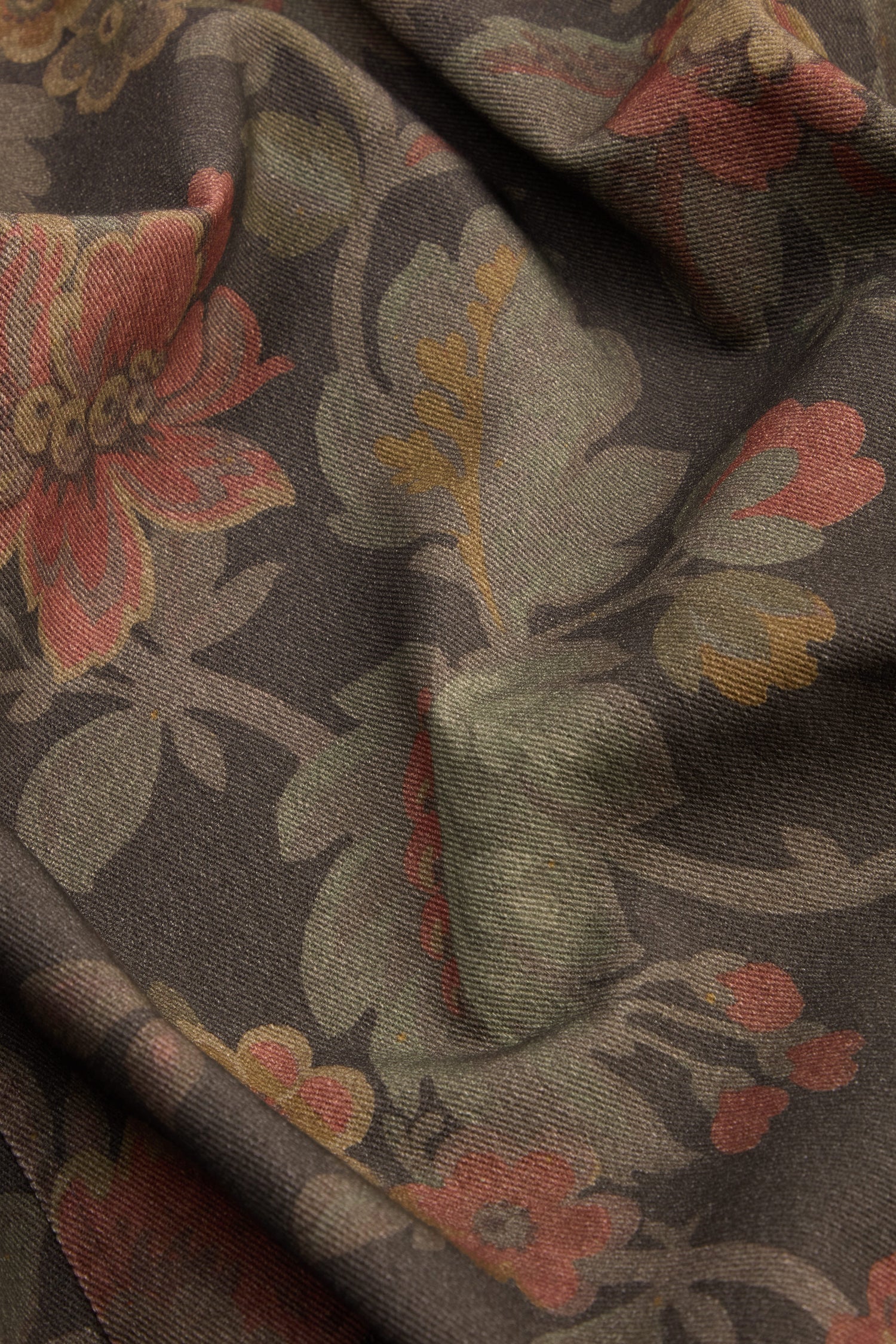 Close-up of brown fabric with a floral pattern in muted red, green, and yellow tones, featuring slight folds and texture—perfect for crafting elegant Heirloom Damask Denim Bubble Trousers.