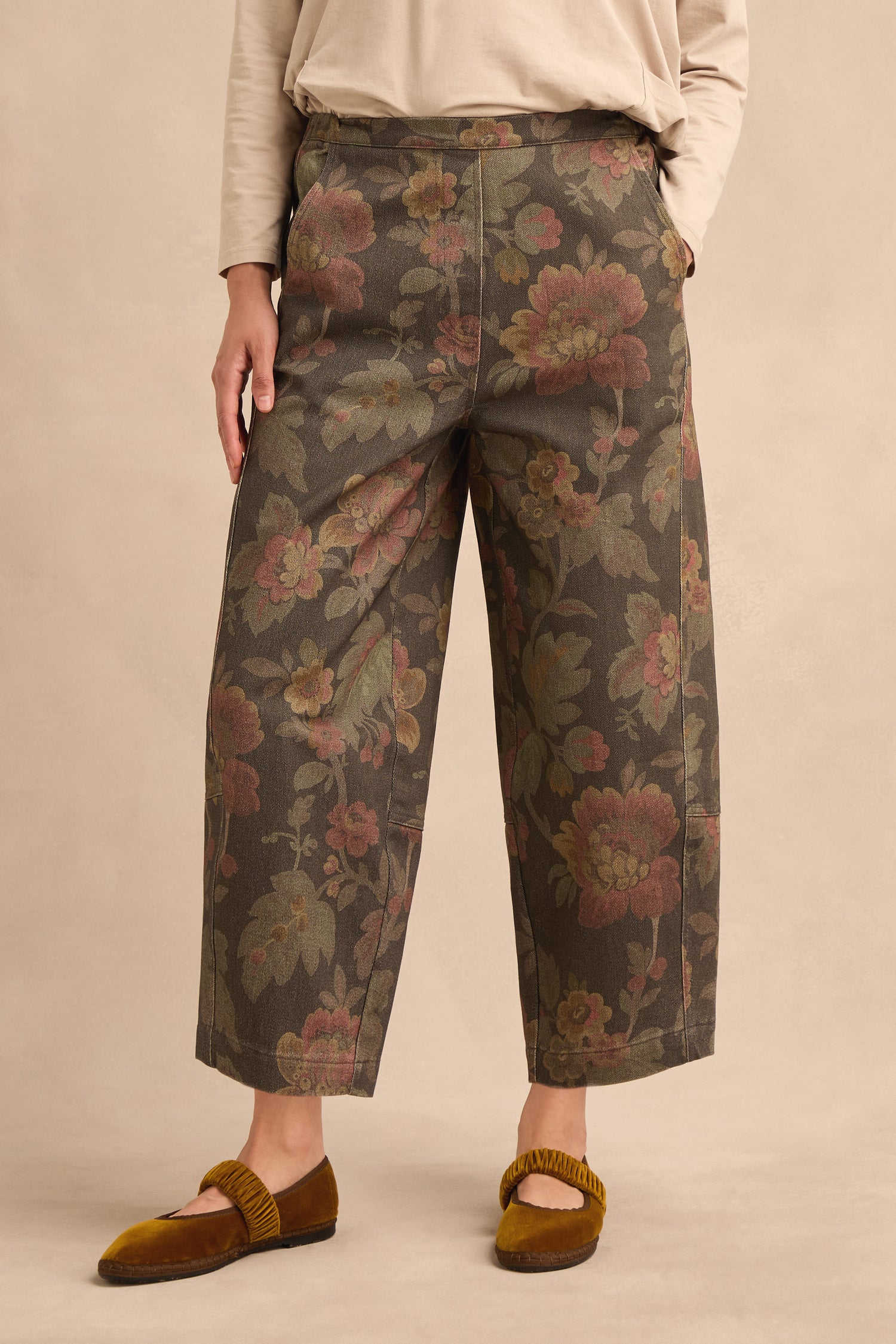 Person wearing Heirloom Damask Denim Bubble Trousers with a wide-leg, cropped silhouette featuring a muted floral pattern, paired with a beige long-sleeve top and brown velvet flat shoes, standing against a neutral background.