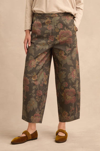 Person wearing Heirloom Damask Denim Bubble Trousers with a wide-leg, cropped silhouette featuring a muted floral pattern, paired with a beige long-sleeve top and brown velvet flat shoes, standing against a neutral background.