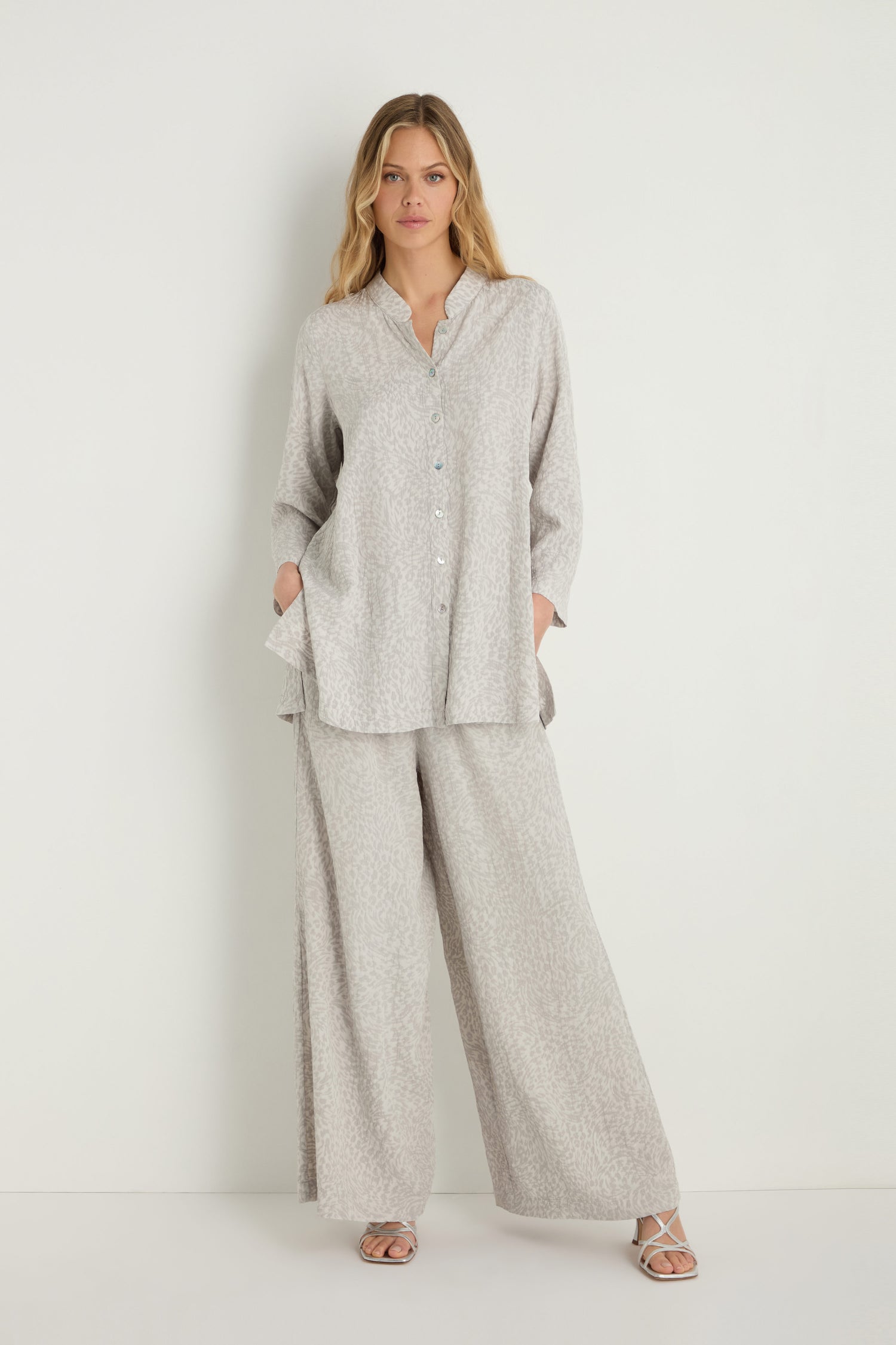 A woman stands against a plain wall with her hands in her pockets, wearing the Animal Textured Jacquard Nehru Shirt and matching wide-leg pants, paired with sandals.