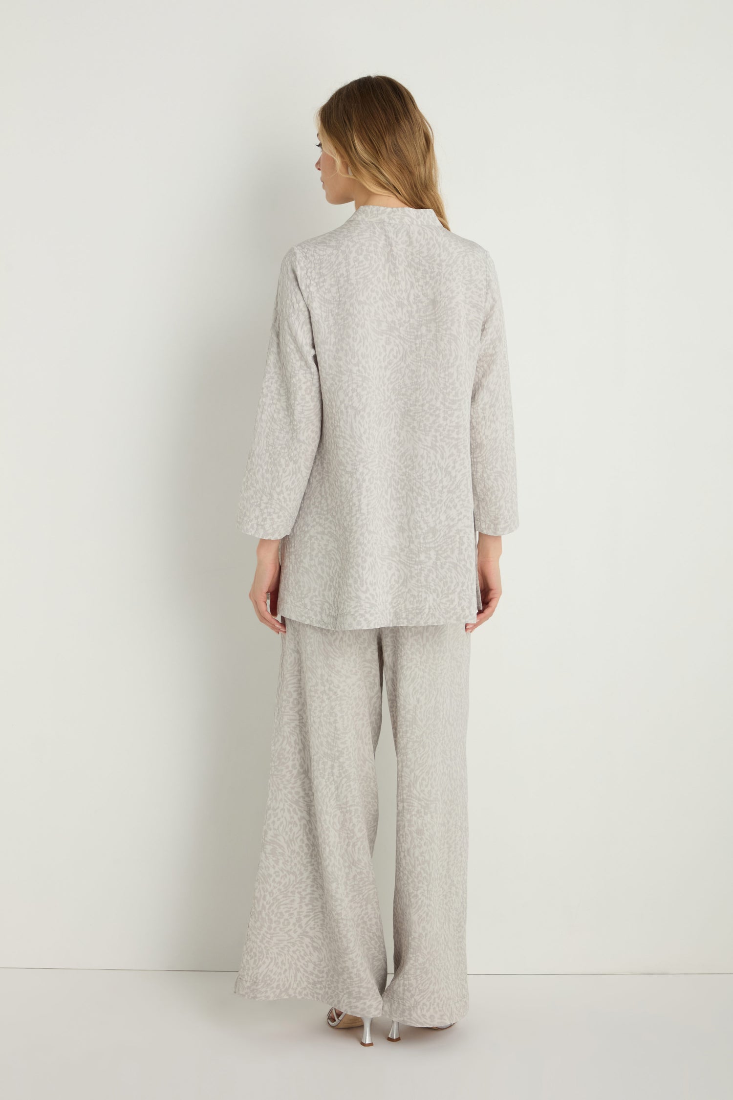 A woman stands facing away, wearing the Animal Textured Jacquard Nehru Shirt in light grey, paired with matching wide-leg pants, set against a plain white background.