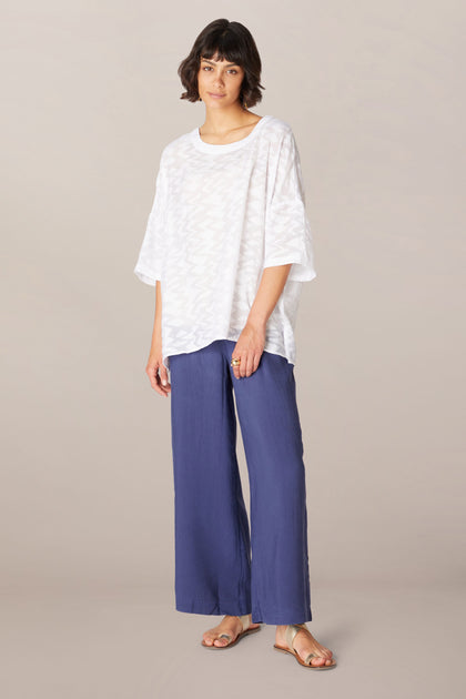 A woman wearing a white relaxed boxy fit Zig Zag Jacquard Top and blue wide leg pants in a Zig Zag Jacquard viscose blend fabric.