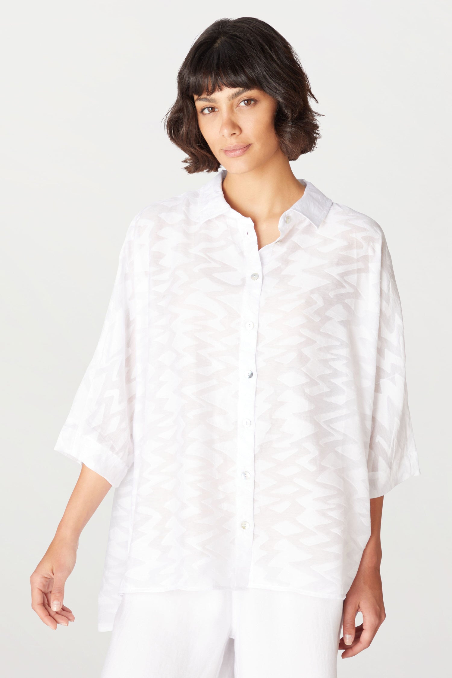A woman dressed in a white Zig Zag Jacquard Shirt and white pants made of a viscose blend fabric adorned with Zig Zag Jacquard pattern.