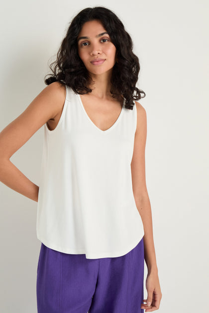 A woman wearing a white Viscose Jersey Flare Vest and purple pants stands against a plain light-colored background.