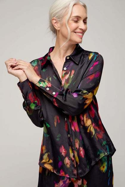 Smiling woman with gray hair wears the Winter Floral Shirt—a black silk blouse featuring a painterly floral print—standing against a plain background with her eyes closed.
