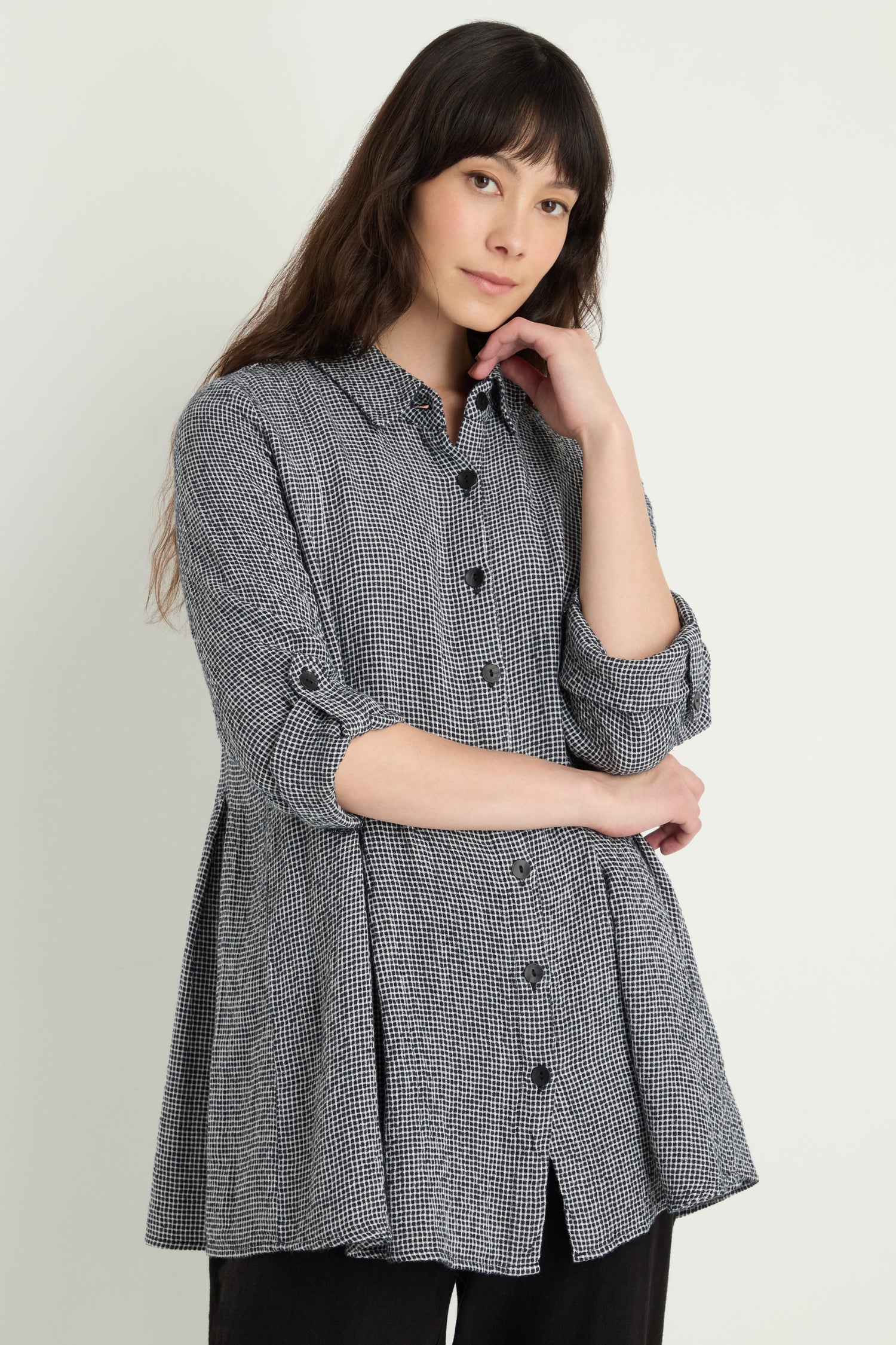 A woman stands against a light background wearing a long-sleeved Micro Gingham Shirt, featuring rolled sleeves and crafted from a linen-viscose blend.