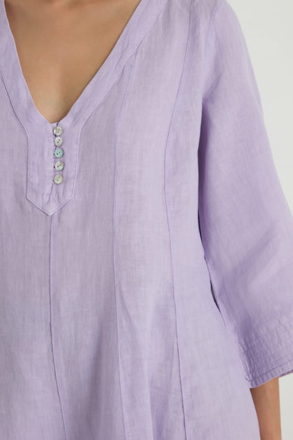 A person wearing the Linen Seam Flare Lilac Tunic, featuring a V-neck, four buttons, and three-quarter sleeves.
