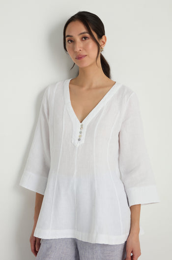 A woman wears the Linen Seam Flare White Tunic, featuring a loose fit, V-neck, button accents, and a gently flared silhouette, standing against a plain light background.