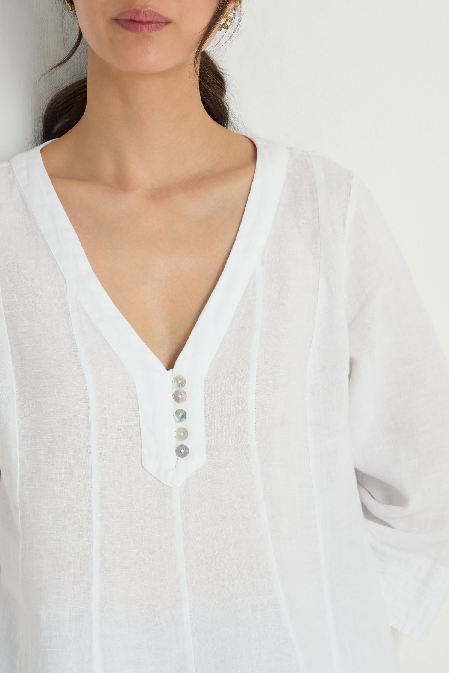 A woman models the Linen Seam Flare White Tunic, featuring three-quarter sleeves and a subtle flare silhouette, photographed from shoulders to chest against a plain background.