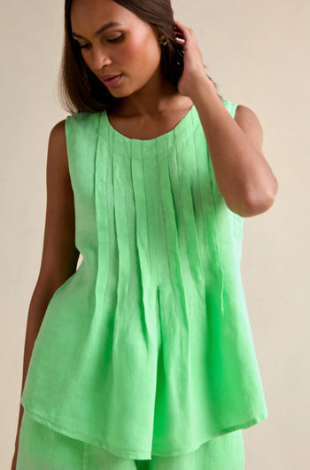 A woman wearing the Linen Pleat Front Pistachio Vest stands against a plain background, touching her hair.