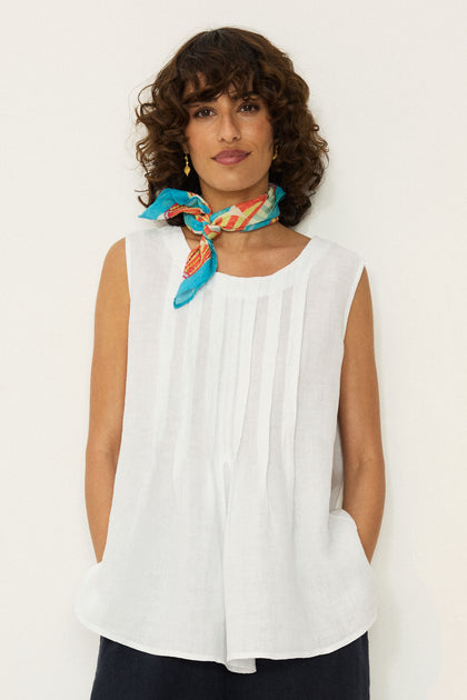 A woman with curly hair wears the Linen Pleat Front White Vest and a colorful scarf, standing against a plain white background with her hands in her pockets.