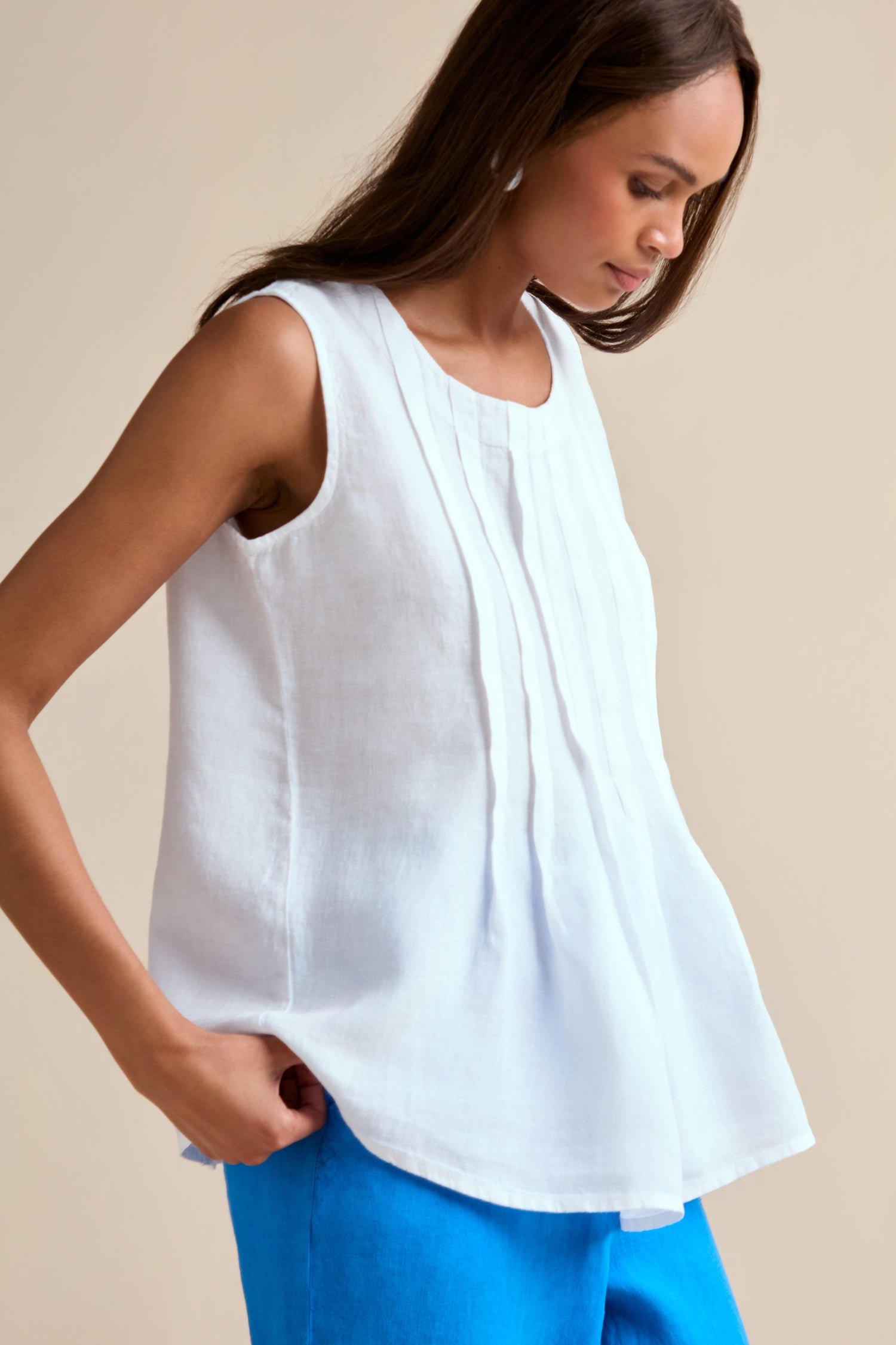 A woman stands against a neutral background wearing the Linen Pleat Front White Vest and vibrant blue pants.