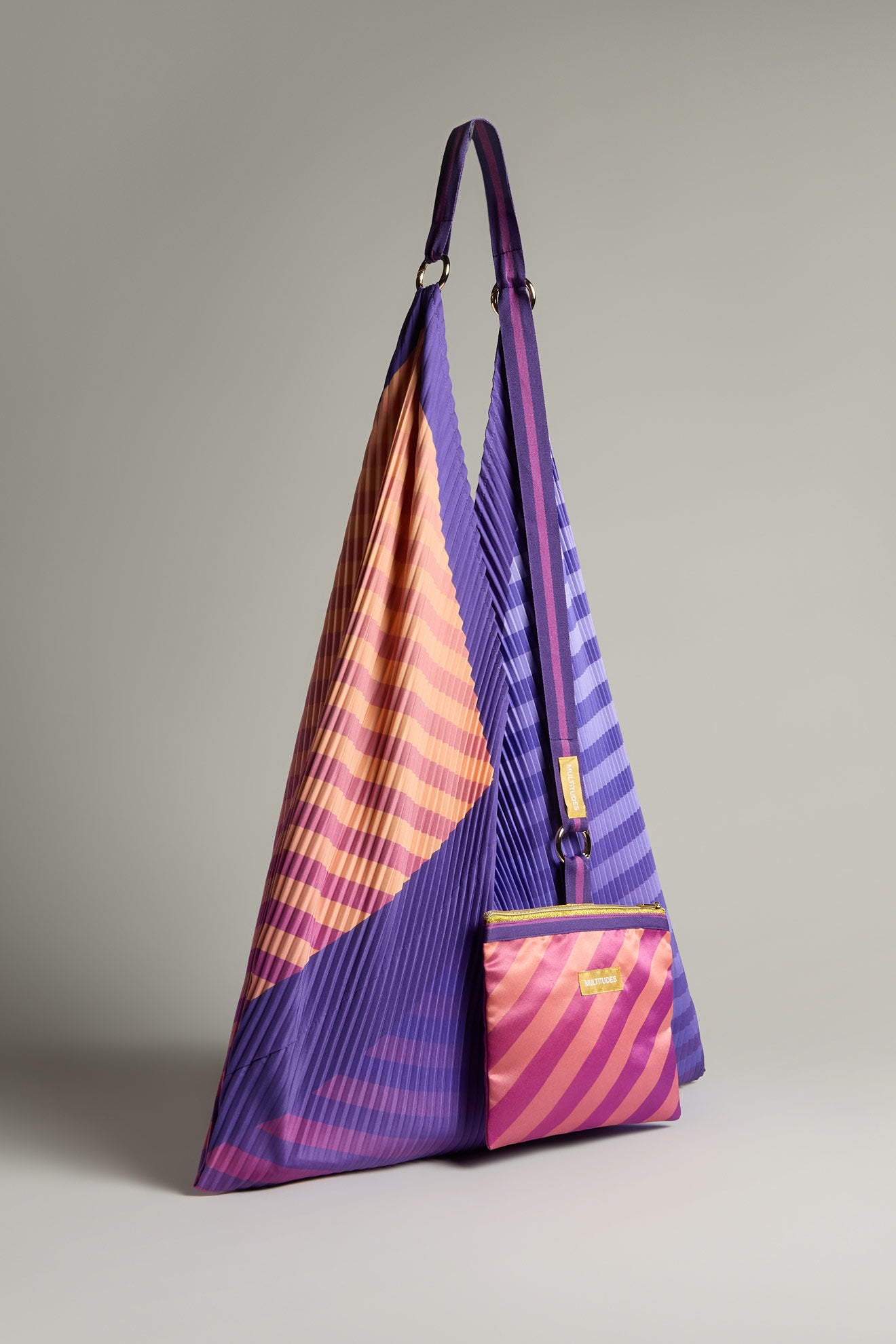 The Pleated Y Handbag, featuring a purple and orange pleated triangular design with a matching crossbody pouch made from recycled materials, is displayed against a plain background. This eco-friendly piece exemplifies sustainable style for today's conscious consumer.