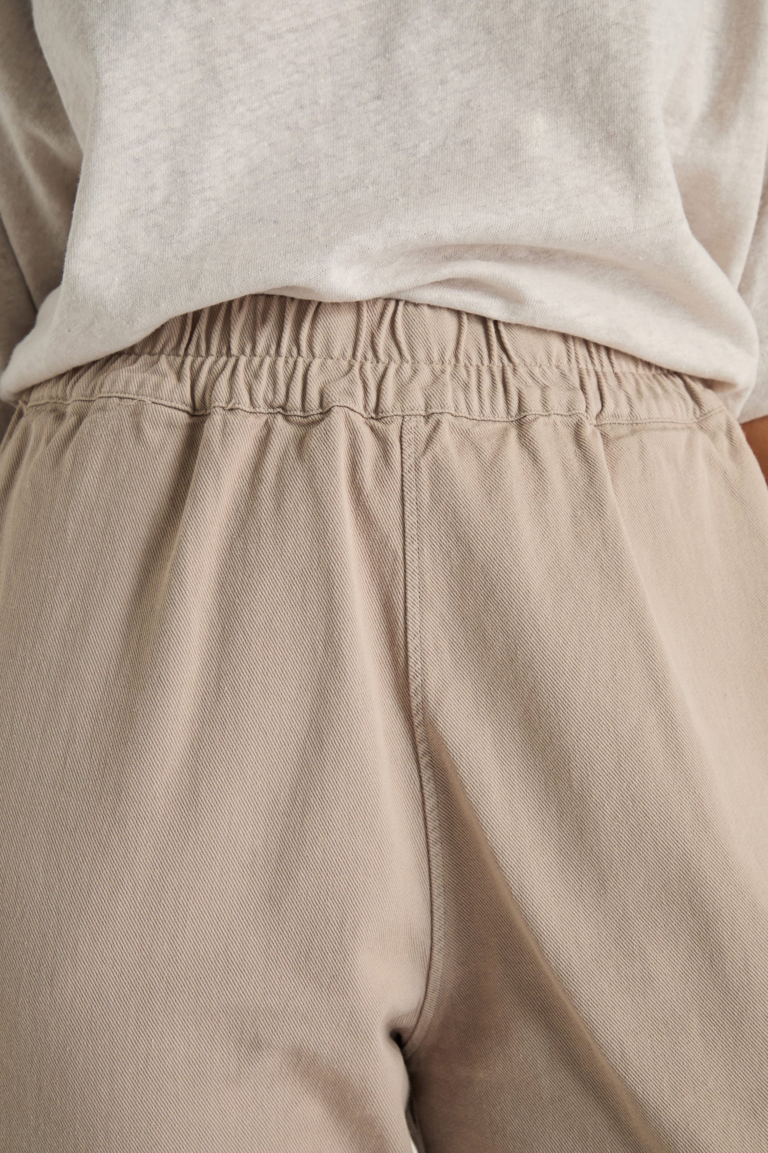 Close-up of a person wearing Heavy Cotton Straight Trousers in light beige, featuring an elasticated waistband and straight leg fit, paired with a light grey t-shirt, highlighting the durable cotton texture.