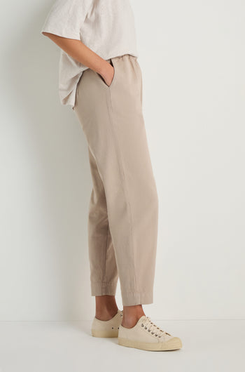 Person standing sideways against a white background, wearing a white short-sleeve shirt, Heavy Cotton Straight Trousers with an elasticated waist and hands in pockets, paired with beige sneakers.