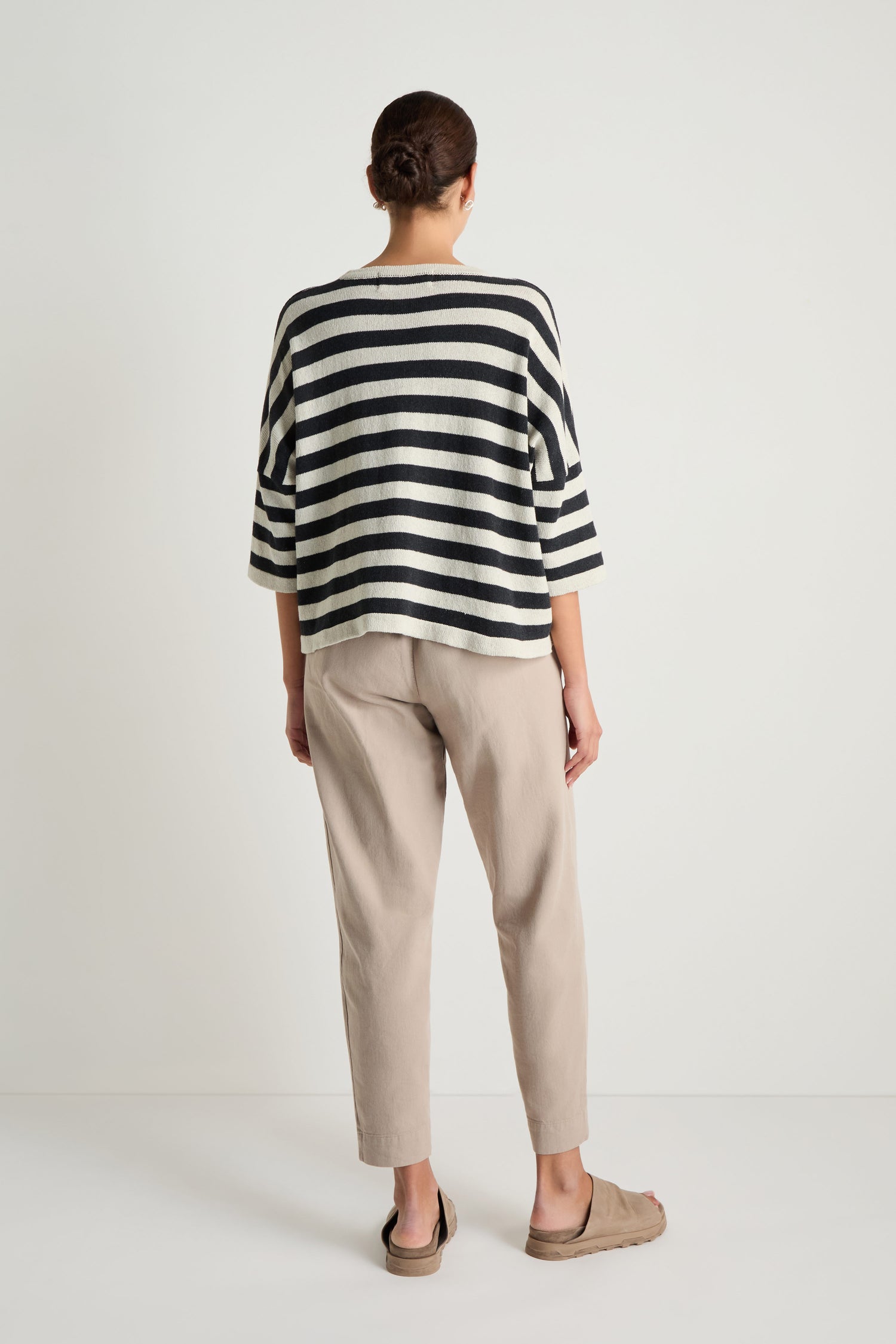 A person stands facing away, wearing the Striped Cotton Knit sweater, beige pants, and tan slip-on shoes against a plain white background.