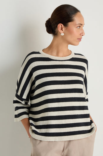 A woman models the Striped Cotton Knit, an oversized sweater, paired with beige pants as she stands with her hands in her pockets against a plain background.