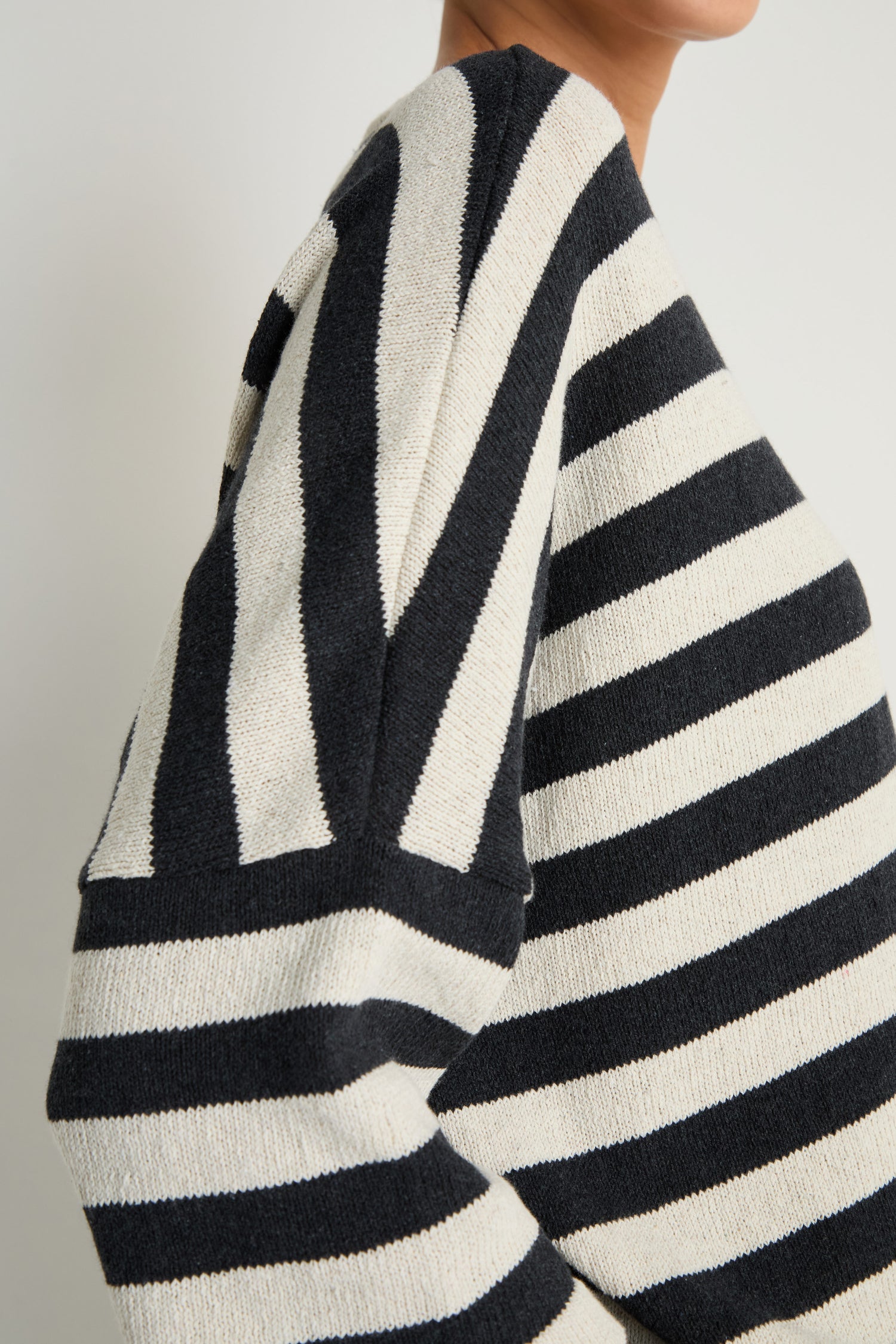 A person wears the Striped Cotton Knit, shown from shoulders to mid-torso against a plain background—a black and white sweater that's a breathable layer for any season.