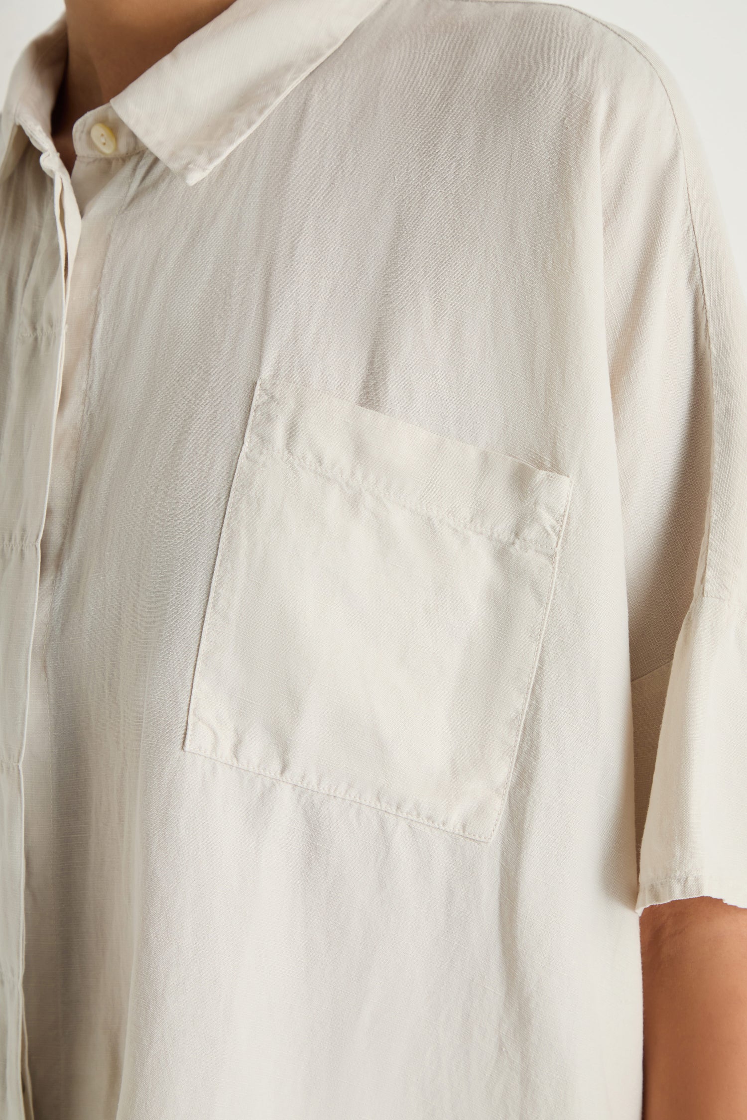Close-up of a person wearing the Lyocell Linen Boxy Shirt, a light-colored top with a chest pocket, shown from shoulder to mid-torso.