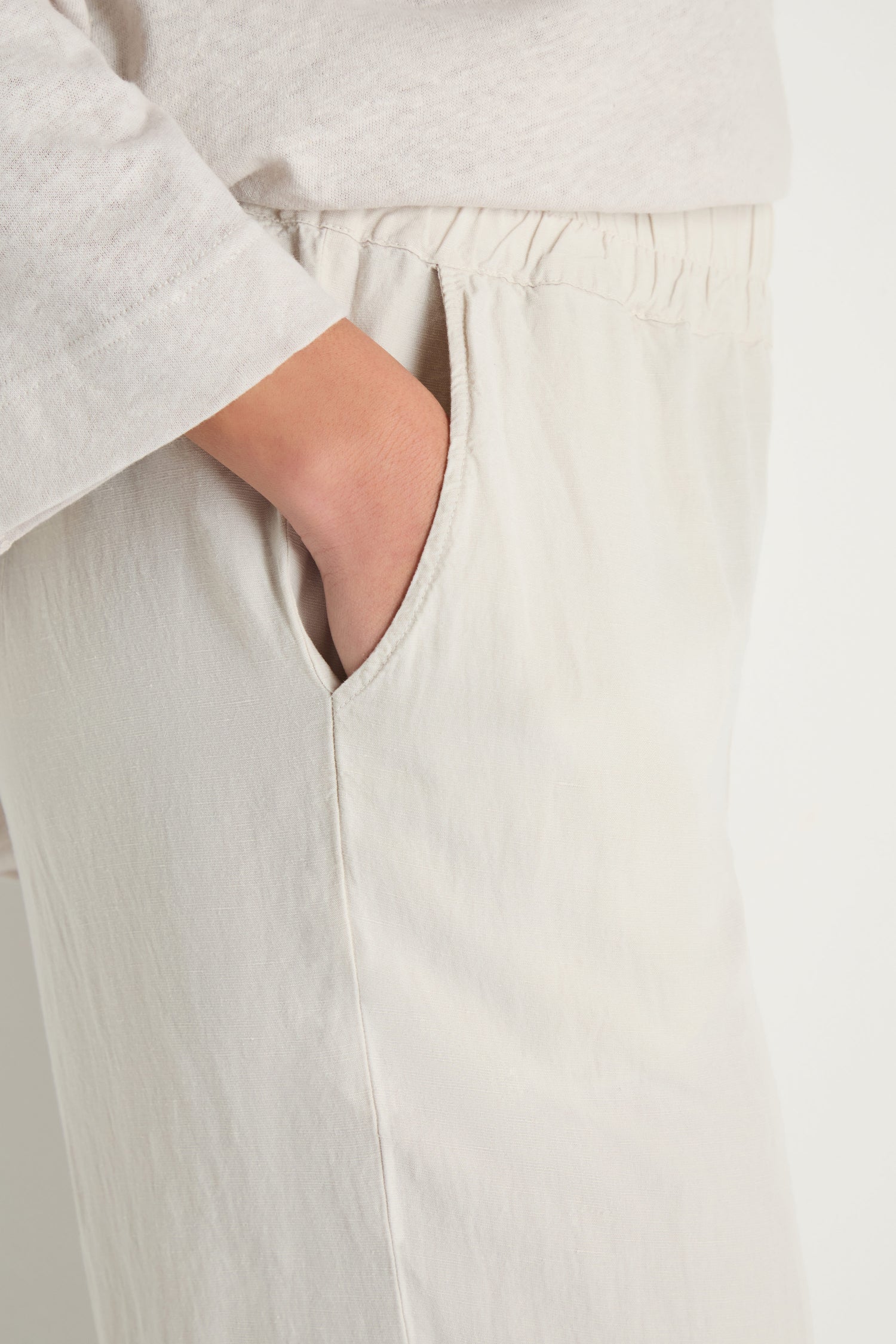 A person wearing Cream Lyocell Linen Slim Trousers with an elasticated waist has their right hand in the pocket.