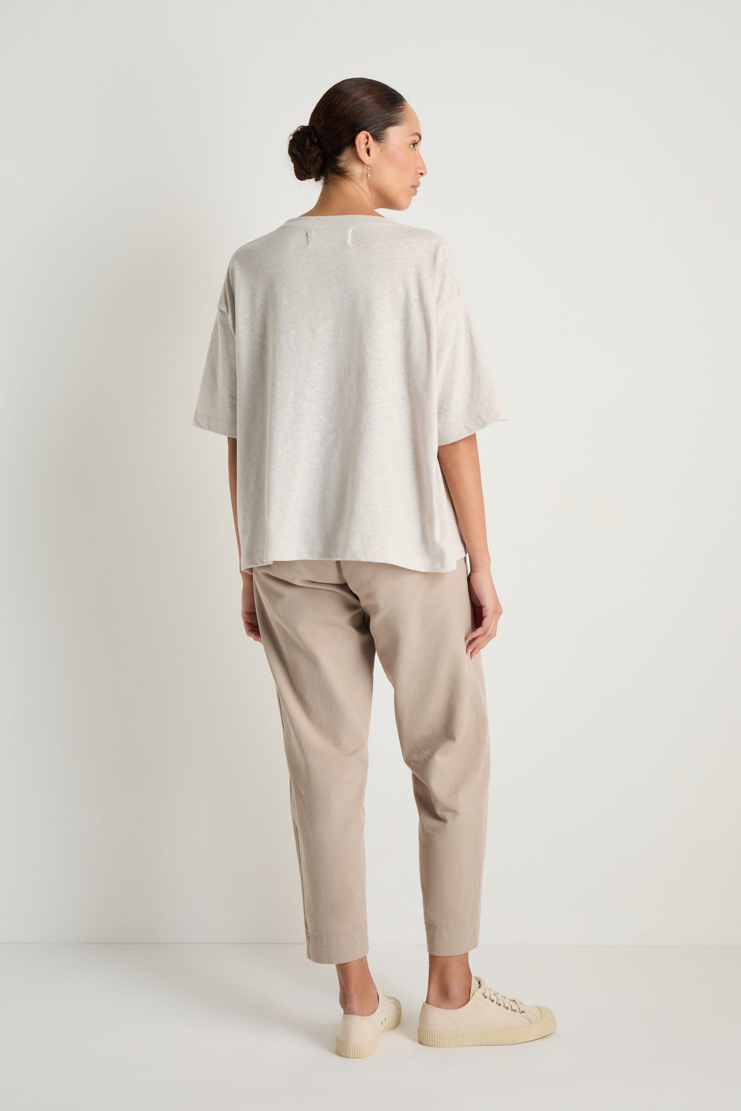 A person faces away, wearing the Linen Cotton Jersey Top in a relaxed fit light beige, paired with tan pants and cream sneakers against a plain white background.