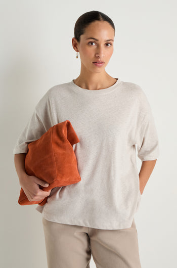 A woman stands against a plain background wearing the Linen Cotton Jersey Top and matching pants, holding a large orange bag under her arm.