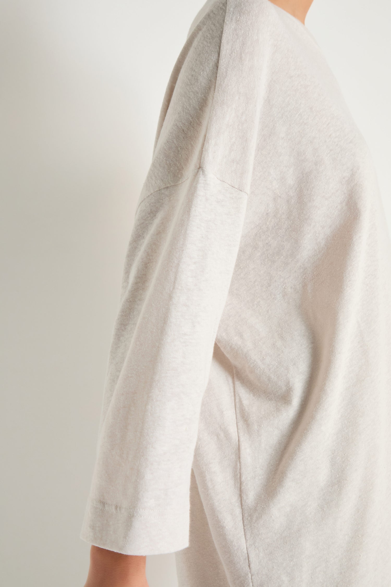 Model in Linen Cotton Jersey Tunic, loose-fitting with dropped shoulders, light beige color, viewed from the side against a plain light background.
